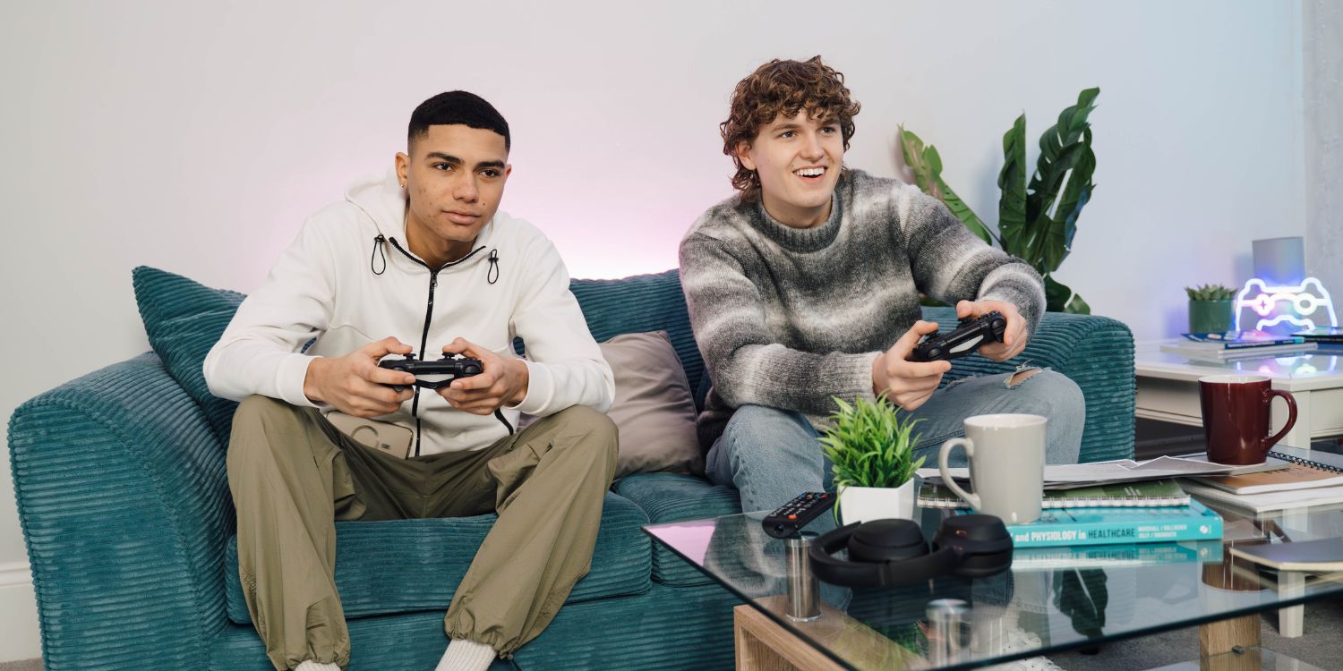 Two students sitting on the sofa gaming online because they've definitely sorted their student broadband on time with a Fused bills package